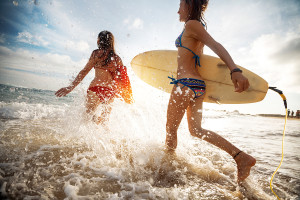 Two young ladies surfers running into sea with surf boards