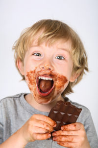 Young messy boy eating a chocolate bar with chocolate on his fac