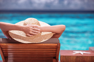 Luxury female tanning on the beach, wearing big stylish hat, enj