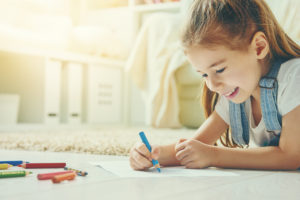 Happy child plays. Little child girl draws with colored pencils.